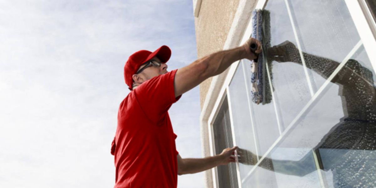 A man in a red shirt diligently cleans a window, showcasing the impact of historic window restoration on home aesthetics.