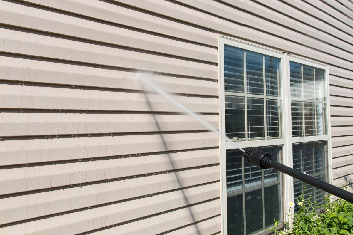 A person operates a pressure washer to clean the exterior of a house, showcasing a professional window cleaning service.