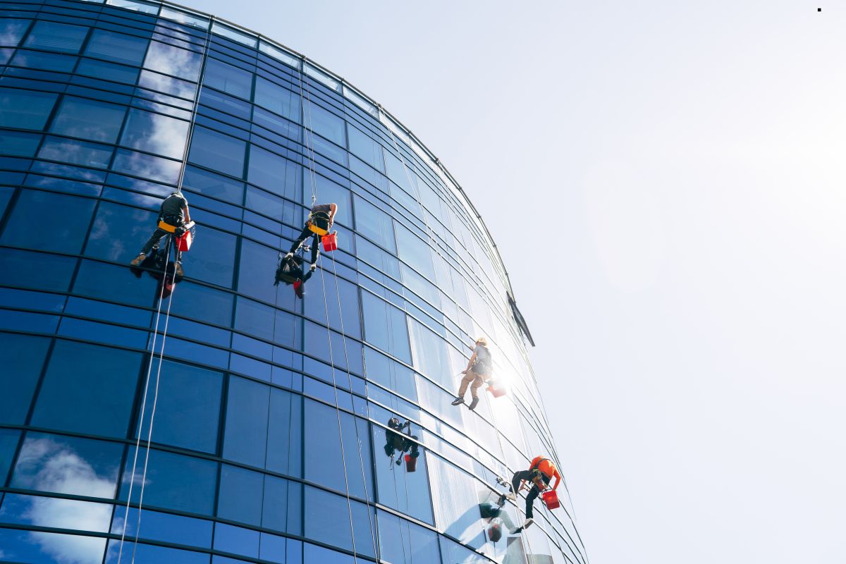 A team of professionals cleaning windows on a high-rise building using ropes for a window cleaning service.