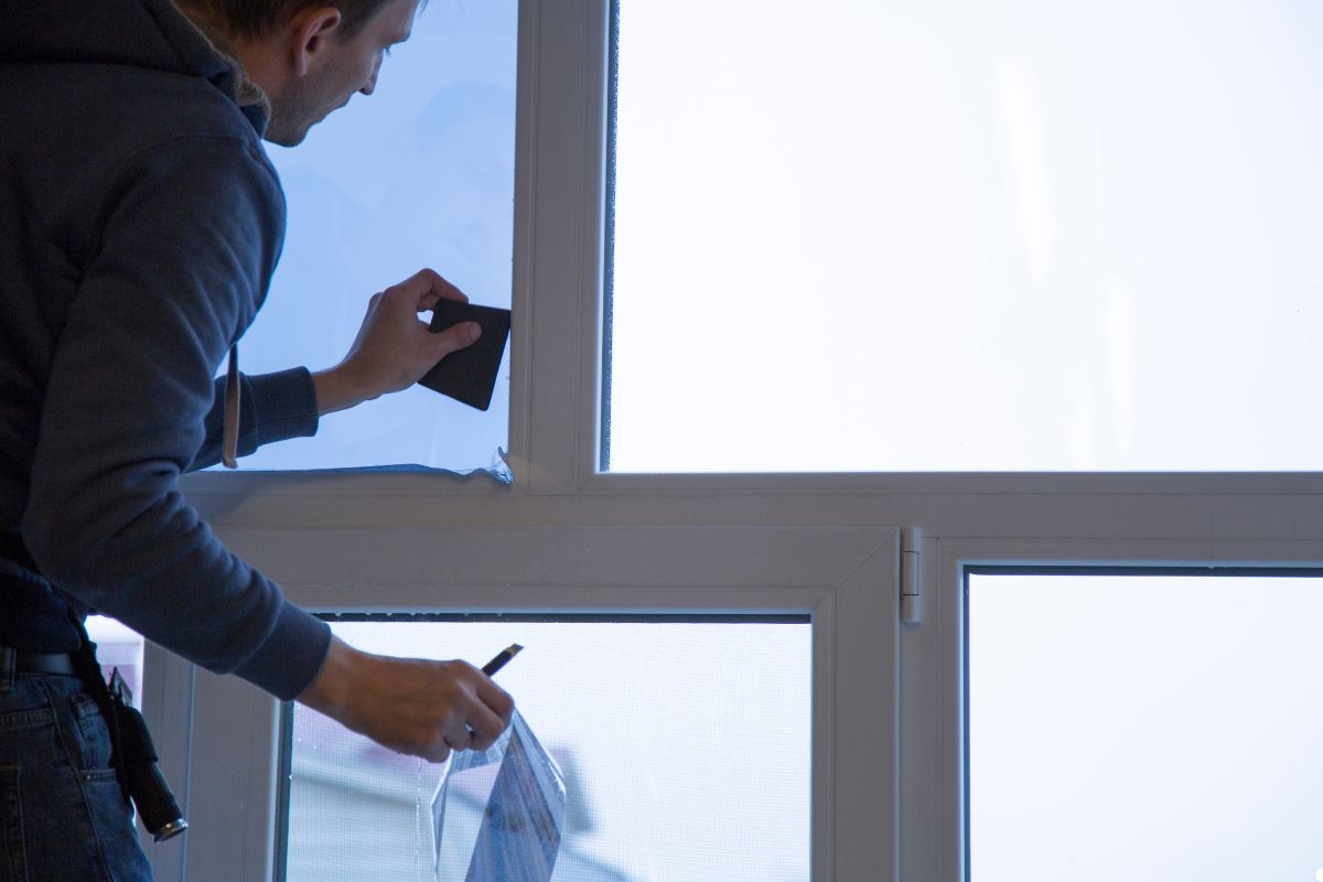 A man applies a window sticker to a glass window, focusing intently on the placement.